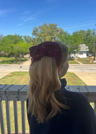 Back view of a burgundy crochet bandana worn over blonde hair outdoors.
