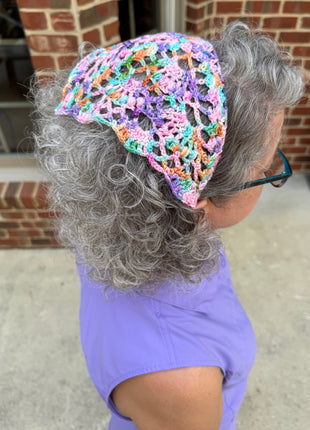 Colorful crochet bandana worn as a head scarf on grey hair.