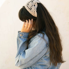 Woman wearing a cream crochet bandana as a head scarf with long dark hair and a denim jacket.