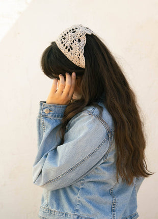 Woman wearing a cream crochet bandana as a head scarf with long dark hair and a denim jacket.