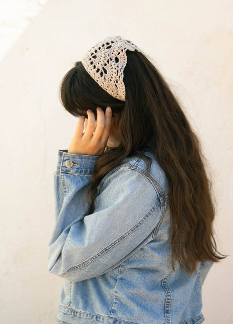 Woman wearing a cream crochet bandana as a head scarf with long dark hair and a denim jacket.