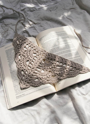 Cream crochet bandana laid on an open book and grey fabric.