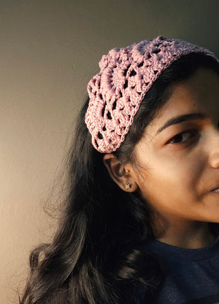 Close-up of a pink crochet bandana worn as a head scarf on dark hair.