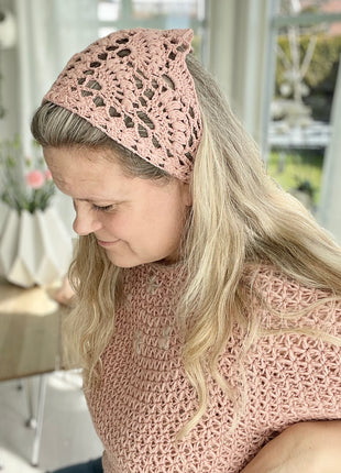 Woman wearing a pink crochet bandana as a head scarf with long blonde hair.