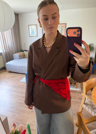 Mirror selfie of a red crochet bandana tied as a waist scarf over a brown jacket.
