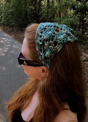 Side view of a teal crochet bandana worn with sunglasses outdoors.