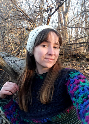 Young woman outdoors wearing a white crochet bandana with a colorful sweater.