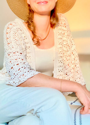 Woman seated while wearing the cream Magnolia Cardigan over a light top.
