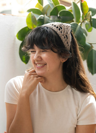 Smiling woman wearing a cream crochet bandana with a white top.